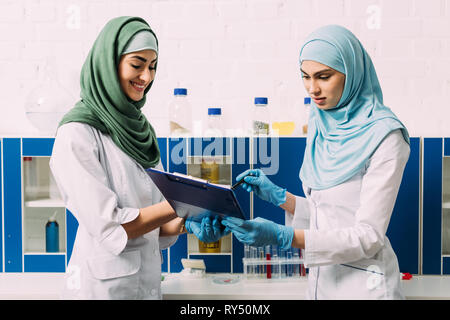 Femmina scienziati musulmani hijab come azienda appunti durante l'esperimento in laboratorio chimico Foto Stock