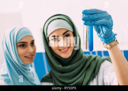 Donna sorridente scienziati musulmani azienda provette in vetro con reagenti durante l'esperimento in laboratorio chimico Foto Stock