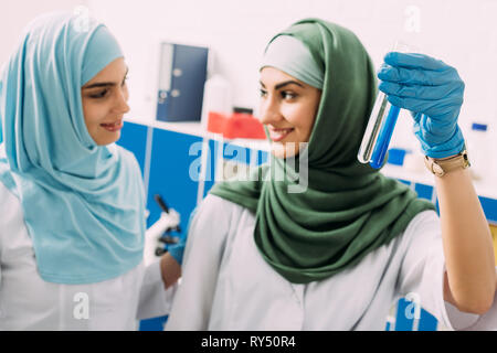 Donna sorridente scienziati musulmani azienda provette in vetro con reagenti durante l'esperimento in laboratorio chimico Foto Stock