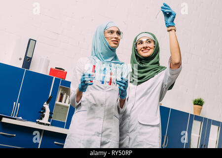 Femmina scienziati musulmani hijab come azienda tubi di test con reagenti durante l'esperimento in laboratorio chimico Foto Stock