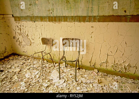 Sedie rotte in un vecchio cariati classroom con vernice cominf fuori le mura in una scuola abbandonata Foto Stock