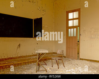 Vintage sedia in legno e la tabella in un vecchio cariati aula con lavagna in una scuola aboned Foto Stock