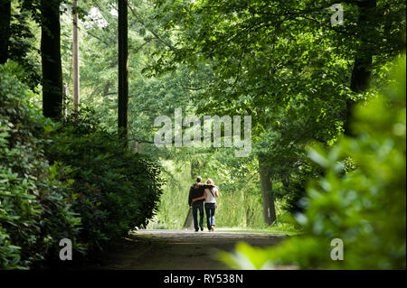 Unges Paerchen laeuft a braccetto durch einen Park in Gladbeck am Wasserschloss Wittringen. Foto Stock