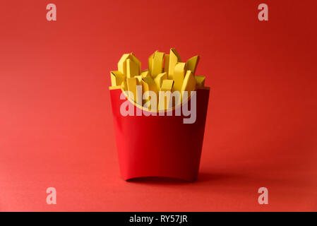 La carta le patatine fritte in rosso scatola di cartone su sfondo rosso. Copia dello spazio. Creative o arte concetto alimentare Foto Stock