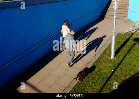 Un uomo con il cane sul piombo getta un ombra come egli cammina attraverso il sottopassaggio Fort William town center Foto Stock