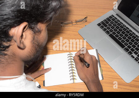 Imprenditore iscritto nel suo diario. Aprire il notebook con pagine vuote accanto alla tazza di caffè e occhiali sul tavolo di legno. Business ancora il concetto di vita WIT Foto Stock
