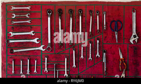 Varie chiavi con delle pinze e forbici disposti sulla parete rossa in officina Foto Stock