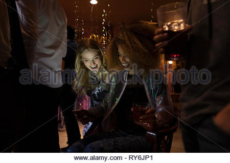 Giovani donne amici utilizzando smart phone in dark night club