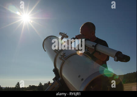Basso angolo vista di astronomo cercando sole luminoso attraverso il cannocchiale contro il cielo chiaro durante la giornata di sole Foto Stock