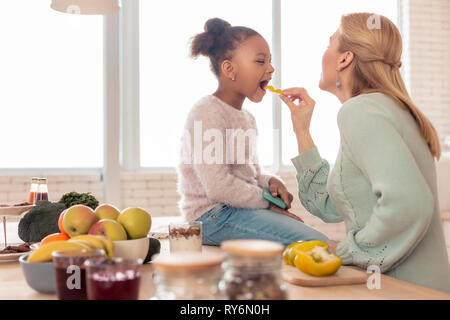 Bionda madre alimentando il suo grazioso funny girl con frutti Foto Stock