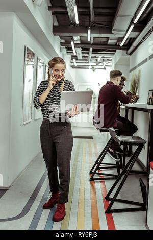 Trasmissione via IR di elegante signora bionda in piedi in corridoio e parlare Foto Stock