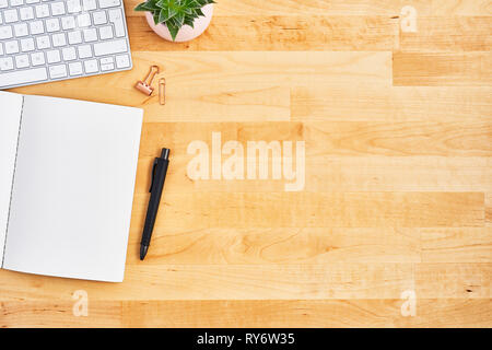 Ufficio di legno scrittoio con notebook vuoto, penna, computer e impianto. Vista dall'alto. Copia spazio per il testo. Lay piatto. Foto Stock