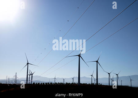 Mulini a vento e tralicci di elettricità sul campo contro il cielo blu e chiaro durante la giornata di sole Foto Stock