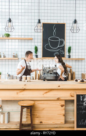 I cassieri in piedi dietro il bancone, parlando e sorridente in coffee house Foto Stock