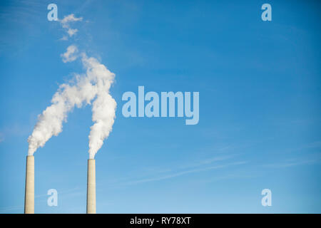 Basso angolo di visualizzazione ad emissione di fumo da camini contro il cielo blu Foto Stock