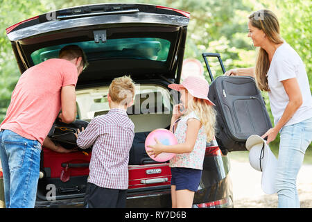 Famiglia con figli insieme imballaggio valigie in auto prima di viaggiare in vacanza Foto Stock