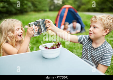 Due i bambini mangiano le ciliegie e bere fuori di tazze mentre camping in natura Foto Stock