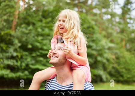 Padre porta figlia piggyback sulle spalle in giardino Foto Stock