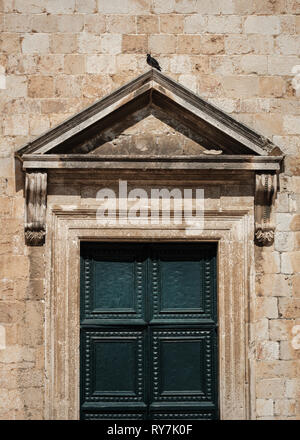 Un vecchio e ornato porta verde situato in una cornice di pietra con un uccello in piedi in cima nella città vecchia main street, Dubrovnik, Croazia Foto Stock