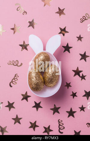Oro glitter uova in un bianco coniglietto di pasqua forma di uovo con orecchie Foto Stock