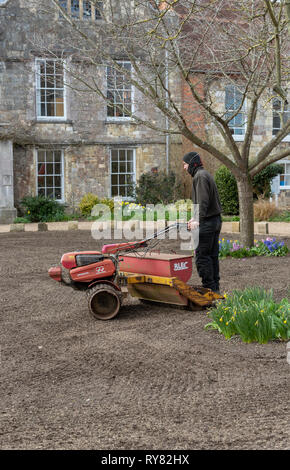 Winchester, Hampshire, Inghilterra England Regno Unito. Marzo 2019. Paesaggio giardiniere a cavallo su un distributore di seme e il rullo per formare un nuovo prato. Foto Stock