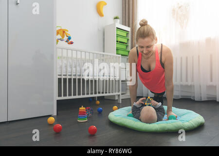 Giovane donna facendo spingere ups a casa mentre si sta giocando con il suo piccolo bambino Foto Stock