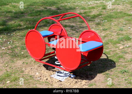 Metallo rosso outdoor parco giochi pubblico attrezzatura in forma di retro vintage ricerca auto pilota a molla con due sedi circondato con erba Foto Stock