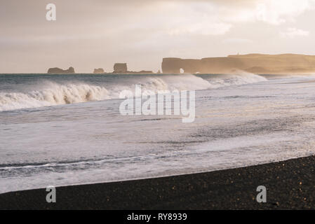 Reynisfjara spiaggia con sabbia nera vulcanica. Vista di Cape Dyrholaey. Una tempesta sul mare con grandi onde. Attrazione turistica di Islanda Foto Stock