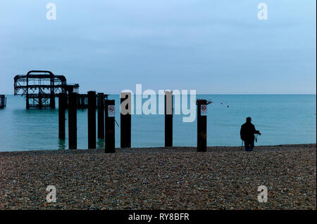 Fotografo sulla spiaggia vicino derelitti Molo Ovest di Brighton Foto Stock