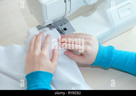 Ragazza caucasica cuce il cotone tessuto bianco sulla macchina da cucire. Close-up. Foto Stock