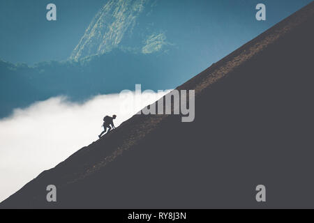 Silhouette di uomo salendo ripida montagna. Morbido e immagine contengono rumore con effetto di filtro adatto per scopo di sfondo solo. Foto Stock