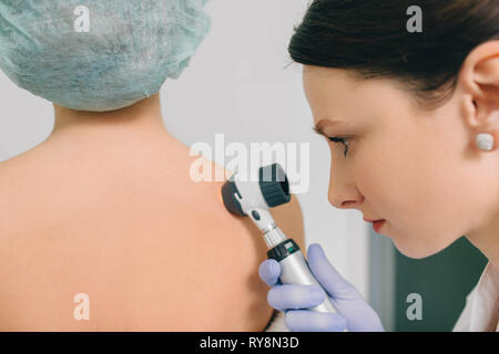 Il dermatologo esamina birthmarks sulla pelle del paziente con un dermatoscope. Dermatologia, pelle mole exam Foto Stock
