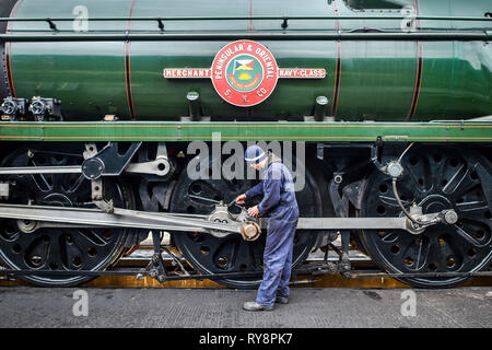 Driver motore Ben Evason versa olio lubrificante in grande parte di estremità della ruota axel di SR ???Marina Mercantile??? Pacific n. 35006 ???Peninsular & Oriental SN Co??? Dall'interno di un pozzetto di ispezione come locomotive sono preparati per il servizio a Gloucestershire Warwickshire Steam Railway Station a Toddington, dove un patrimonio speciale di vapore treno express service sta prendendo i frequentatori di gara per Cheltenham. Foto Stock