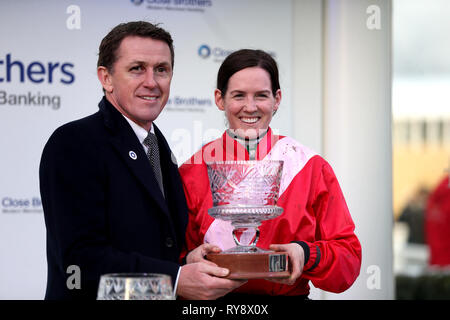 Jockey Rachael Blackmore è presentato con il suo trofeo da una P McCoy dopo aver vinto il vicino Fratelli novizi' Handicap Chase su un Plus Tard campione durante il giorno del 2019 Cheltenham Festival a Cheltenham Racecourse. Foto Stock