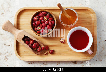 Vista superiore della deliziosa rosa anca tè in tazza con secchi rosa canina sul vassoio in legno Foto Stock