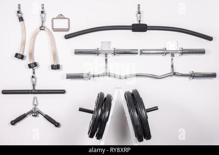 Palestra marce appeso a una parete. Piastre di peso, curl bar e diverse maniglie, funi e le aste / barre per macchine via cavo. Foto Stock