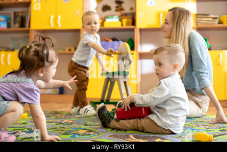 Vivaio di neonati con il mentor giocando in kindergarten Foto Stock