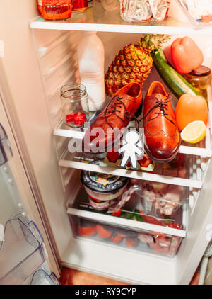 Da sopra la silhouette di carta per il giorno di sciocchi di aprile nei pressi di scarpe, uova nel contenitore e cibo su scaffali in frigorifero Foto Stock