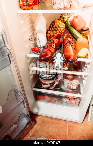 Da sopra la silhouette di carta per il giorno di sciocchi di aprile nei pressi di scarpe, uova nel contenitore e cibo su scaffali in frigorifero Foto Stock