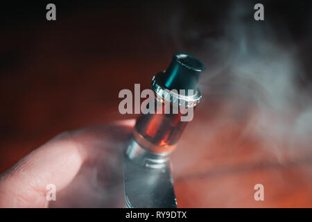 L'uomo azienda vape metallo pen sigaretta elettronica con vaping nuvola di fumo scuro dello sfondo Foto Stock