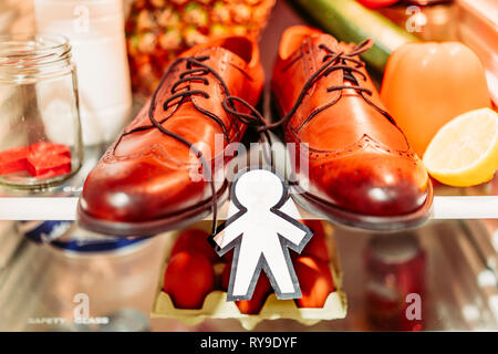 Da sopra la silhouette di carta per il giorno di sciocchi di aprile nei pressi di scarpe, uova nel contenitore e cibo su scaffali in frigorifero Foto Stock