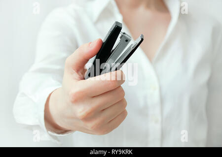 Ragazza caucasica in una camicia bianca tiene in mano un nero cucitrice per carta. Close-up. Foto Stock