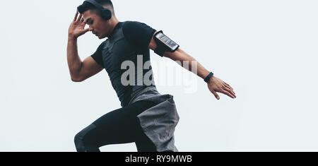 Montare uomo asiatico facendo allenamento. Giovane uomo asiatico in nero abbigliamento sportivo stretching con cuffie e mobile su fascia braccio. Foto Stock