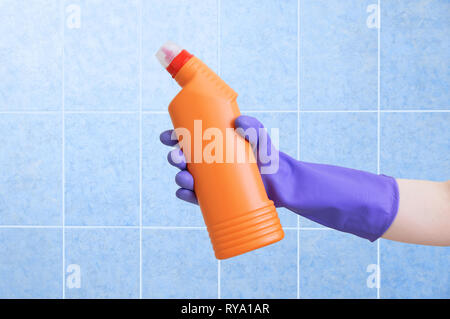 Mano nel guanto protettivo. Prodotti chimici di uso domestico in mano. Blue Sfondo piastrelle. Foto Stock