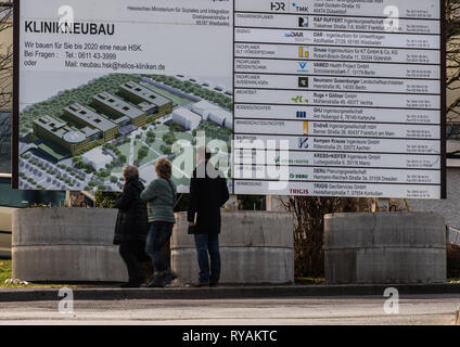 Wiesbaden, Germania. Xii Mar, 2019. Tre persone guardano il segno di costruzione per i motivi del 'Dr.-Horst-Schmidt-Klinik". L'operatore, Helios Verwaltung Hessen GmbH, piani per completare una nuova clinica edificio dal 2021, con un investimento di 268 milioni di euro. Credito: Andreas Arnold/dpa/Alamy Live News Foto Stock