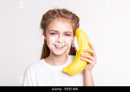 Sorridente bella piccola signora mantenendo big orange fake banana Foto Stock