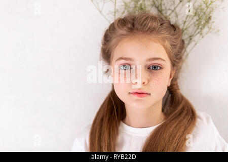 Graziosa bambina con viso carino giacente sul piano con fiori Foto Stock