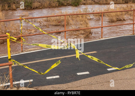 Giallo rotto Nastro di avvertenza torsioni del vento durante l'acqua alta evento in Tucson, normalmente secca Rillito il letto del fiume Foto Stock