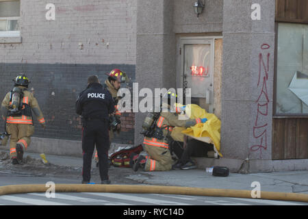 Hamilton, Canada 2019: Vigili del fuoco e polizia di occuparsi di una vittima di inalazione di fumo dopo un edificio con appartamenti fire. Il salvataggio di persone da un incendio. Foto Stock