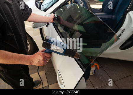 La procedura guidata per l'installazione di apparecchiature aggiuntive bastoni una tinta pellicola sul lato vetro anteriore della vettura e asciugare il vetro con un essiccatore industriale presso il Foto Stock